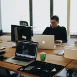 A web developer working on code in a modern office setting with multiple devices.