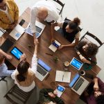 Top view of a diverse team collaborating in an office setting with laptops and tablets, promoting cooperation.